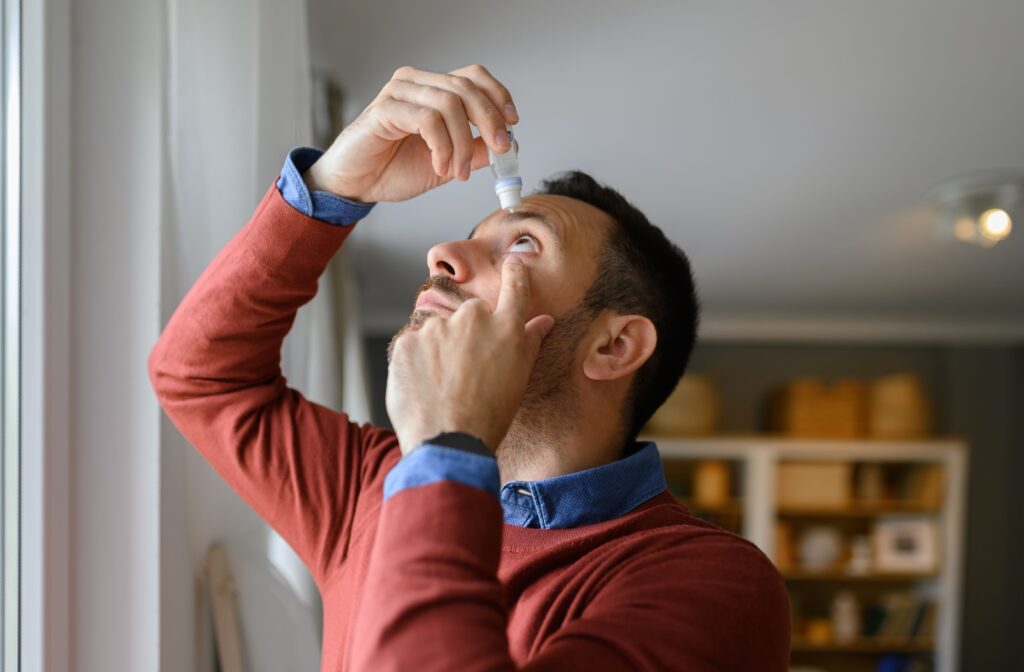 A man looking up and holding his left eye open with his left hand while putting eye drops with his right hand.