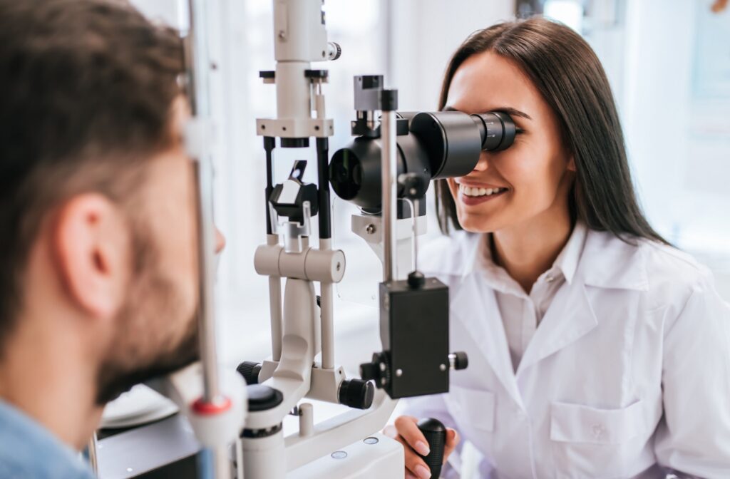 A young female optometrist smiling while examining a male patient's eyes during an eye exam.