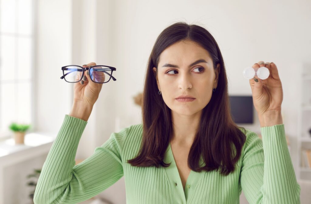 A prescription eyewear user holding up contact lenses & eye glasses, comparing the two.