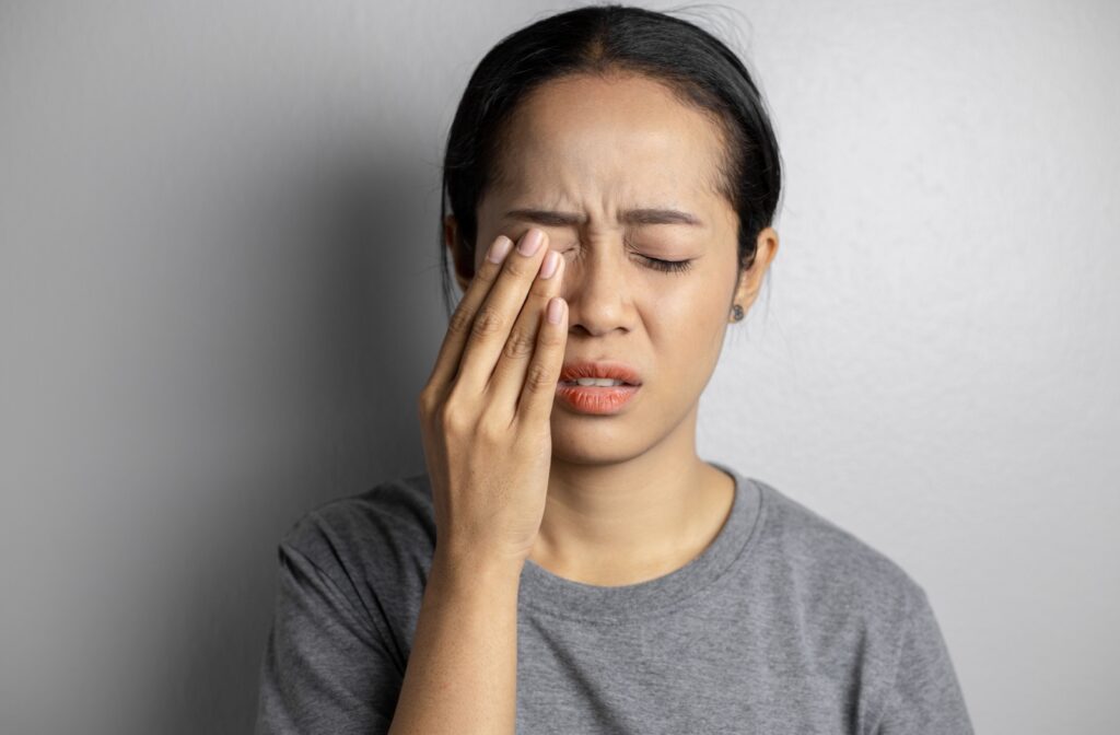 A young woman holds a hand against her scratched eye with a pained expression on her face.