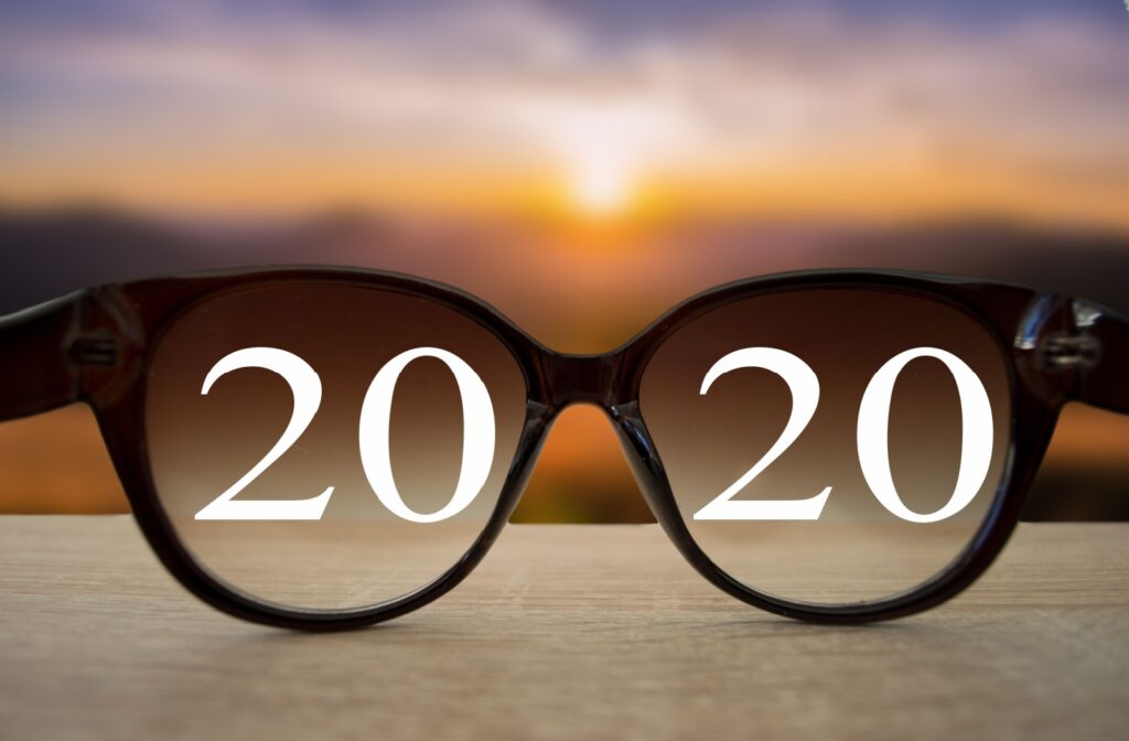 An image of looking through a pair of glasses towards a sunset, with the numbers 20 20 displayed within the frame of the glasses signifying perfect vision.