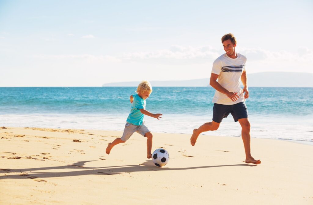 A father and young son playing soccer on the beach, enjoying outdoor time away from screens to support healthy boundaries for eye health.