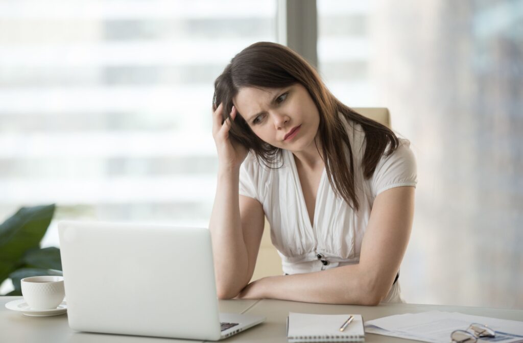 A woman sitting at a desk, looking at her laptop with a confused and slightly strained expression, due to double vision.