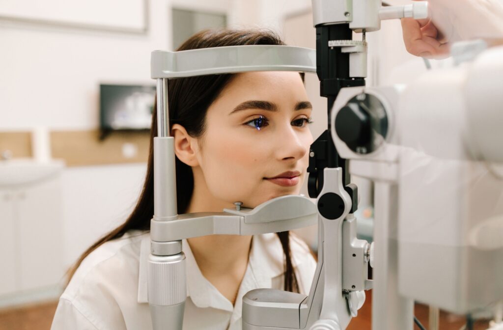 Patient with dilated pupils undergoing an eye exam, head positioned in a diagnostic tool with a laser.