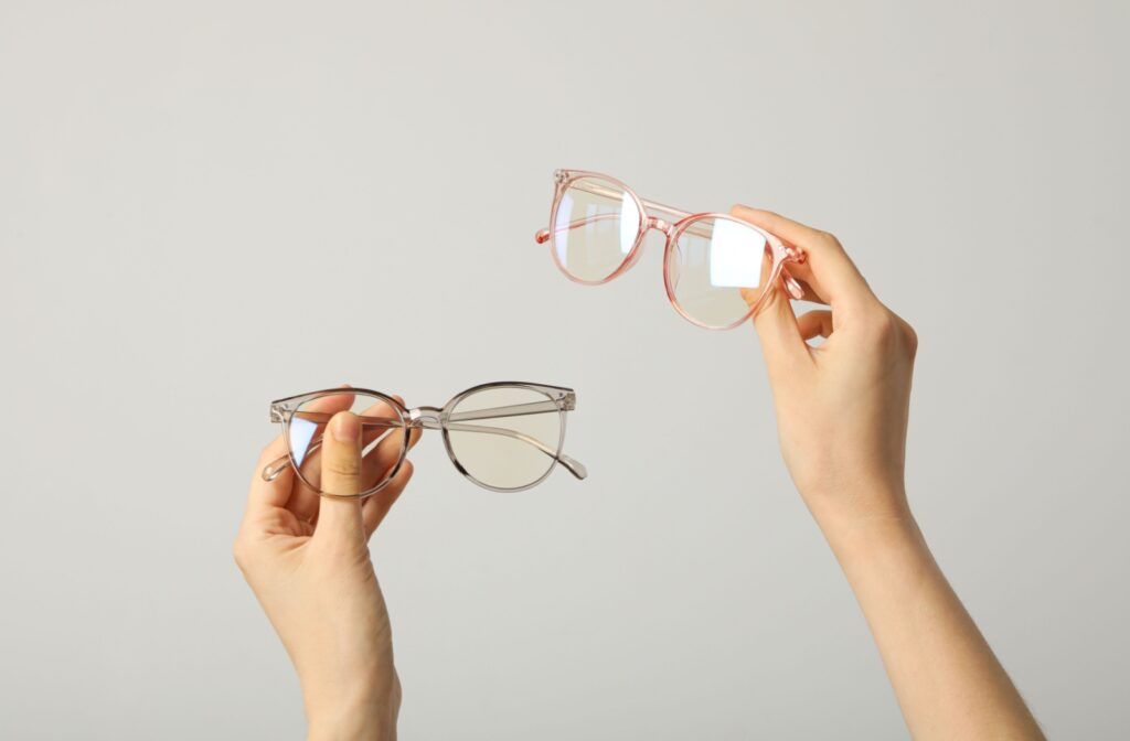 Hands holding up two pairs of glasses with anti-reflective coating on the lenses.