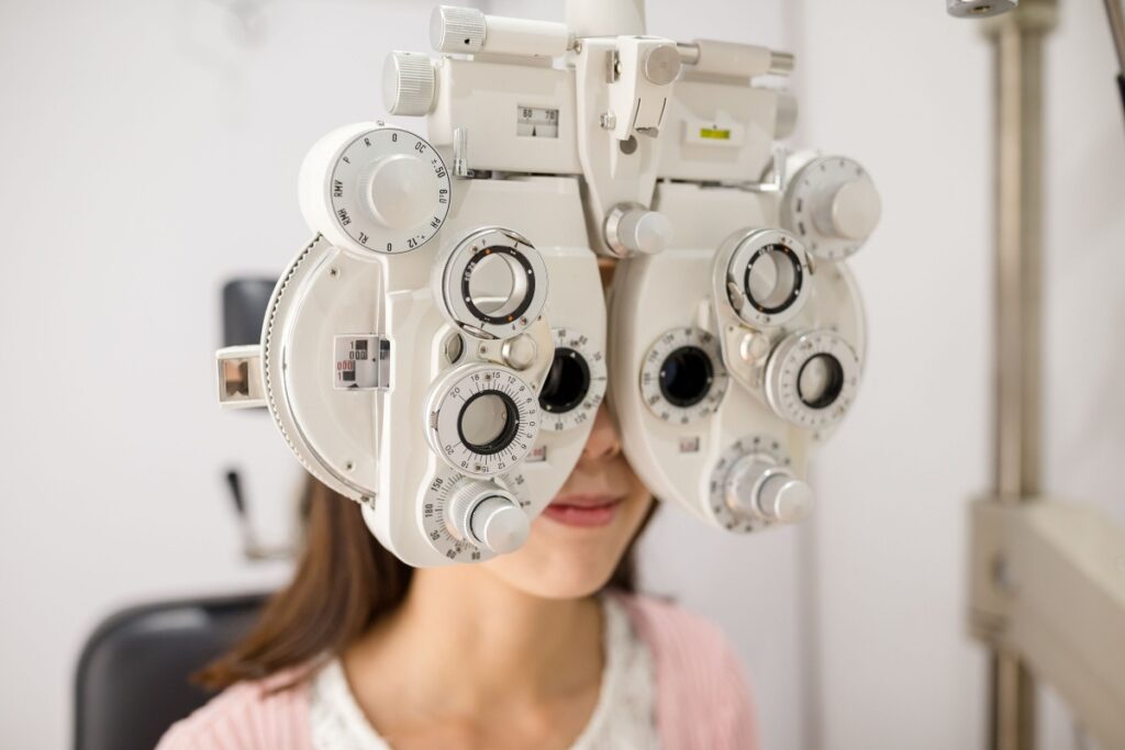 A person looking through a phoropter at an annual eye exam to monitor overall eye health.