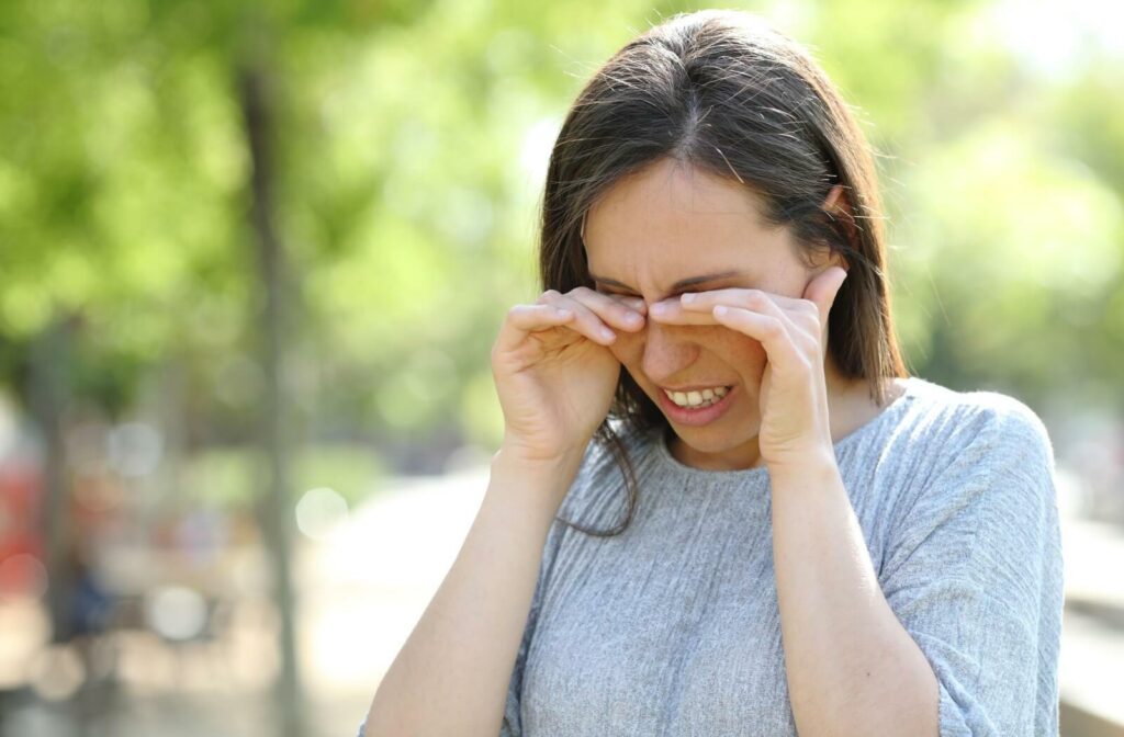 A person outside, holding their eyes due to allergies affecting their vision.